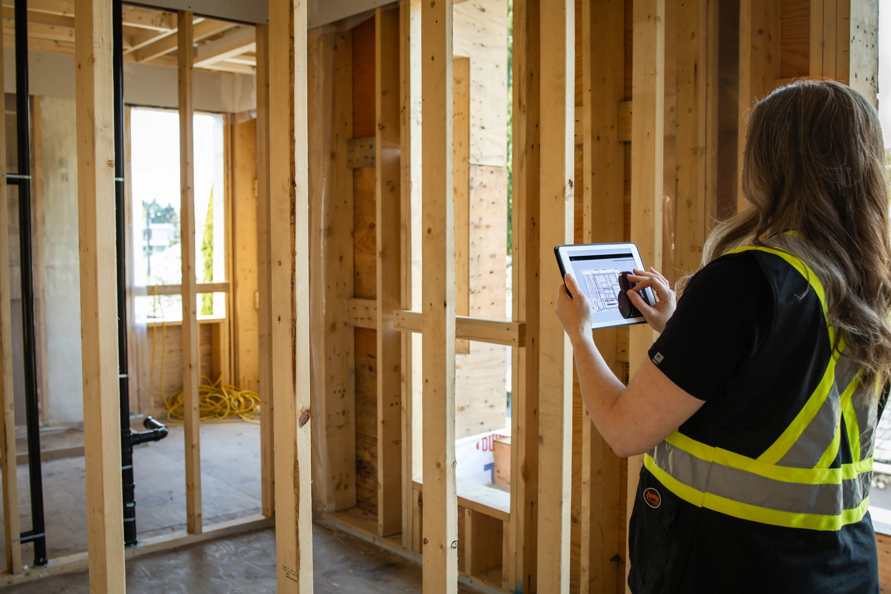 Rebecca Sorbara reviewing building plans on a tablet inside a wood-framed residential construction site in Vancouver